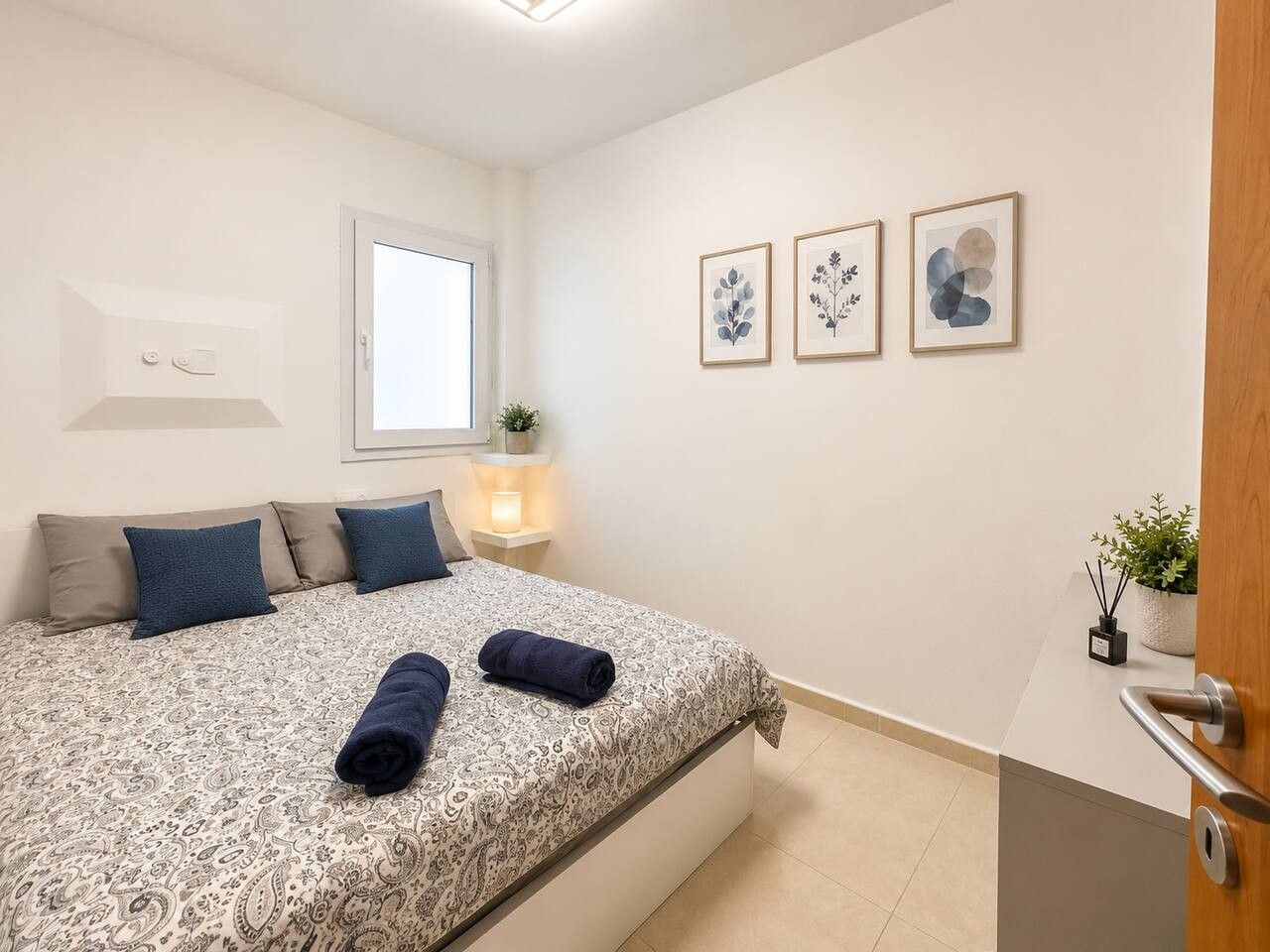 Une chambre à coucher avec un lit, des oreillers, une table de chevet avec une lampe et des œuvres d’art encadrées accrochées au mur.