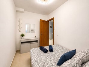 Un dormitorio con cama, dos almohadas, una mesita de noche, un espejo, un armario y una pequeña planta.