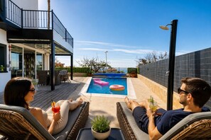 Zona de piscina con sillones de descanso y un área de estar techada.