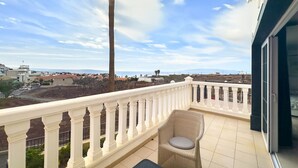 Un balcon doté d’une balustrade blanche, d’une chaise en osier et offrant une vue sur un paysage côtier.
