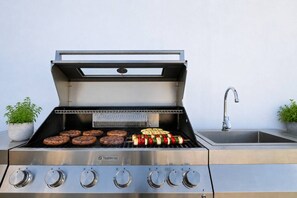 A stainless steel outdoor grill with multiple burners, a built-in thermometer, and a side sink.