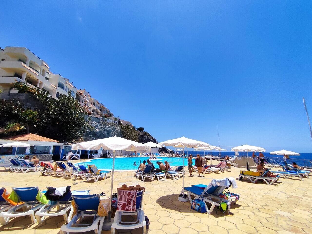 A beachside hotel with a pool, sun loungers, and umbrellas.
