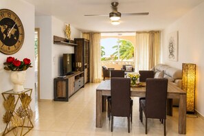 Une chambre d’hôtel avec un coin repas, une télévision, un ventilateur de plafond et une vue sur les palmiers.