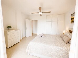 Une chambre à coucher comprenant un lit, une commode, un ventilateur de plafond et une porte donnant sur une autre pièce.