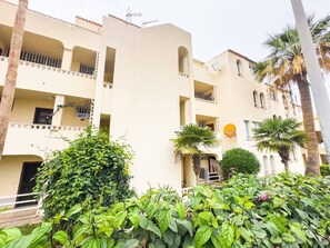 Un immeuble à plusieurs étages doté de balcons, d’une antenne parabolique et d’une végétation luxuriante au premier plan.