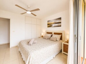 Une chambre à coucher comprenant un lit, des tables de chevet, un ventilateur de plafond, un tableau et une porte coulissante.