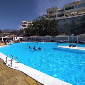 Une piscine où l’on voit des personnes, entourée d’immeubles et d’arbres.