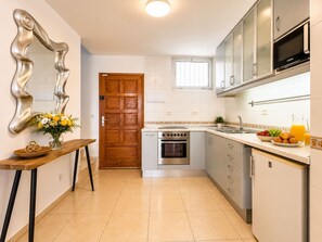 Une cuisine équipée d’un four encastré, d’un four à micro-ondes et d’un évier. On y trouve une porte en bois et une fenêtre située au-dessus de l’évier.