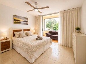 Une chambre à coucher comprenant un lit, des tables de chevet, un ventilateur de plafond, une fenêtre avec des rideaux, un canapé et un meuble de rangement.