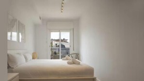 Une chambre à coucher avec un lit, une table de chevet et une fenêtre donnant sur les bâtiments environnants.