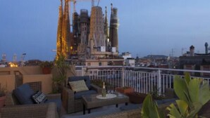 Une terrasse sur le toit, aménagée avec des meubles en osier, des plantes en pot et offrant une vue sur le paysage urbain, avec ses grues de chantier.