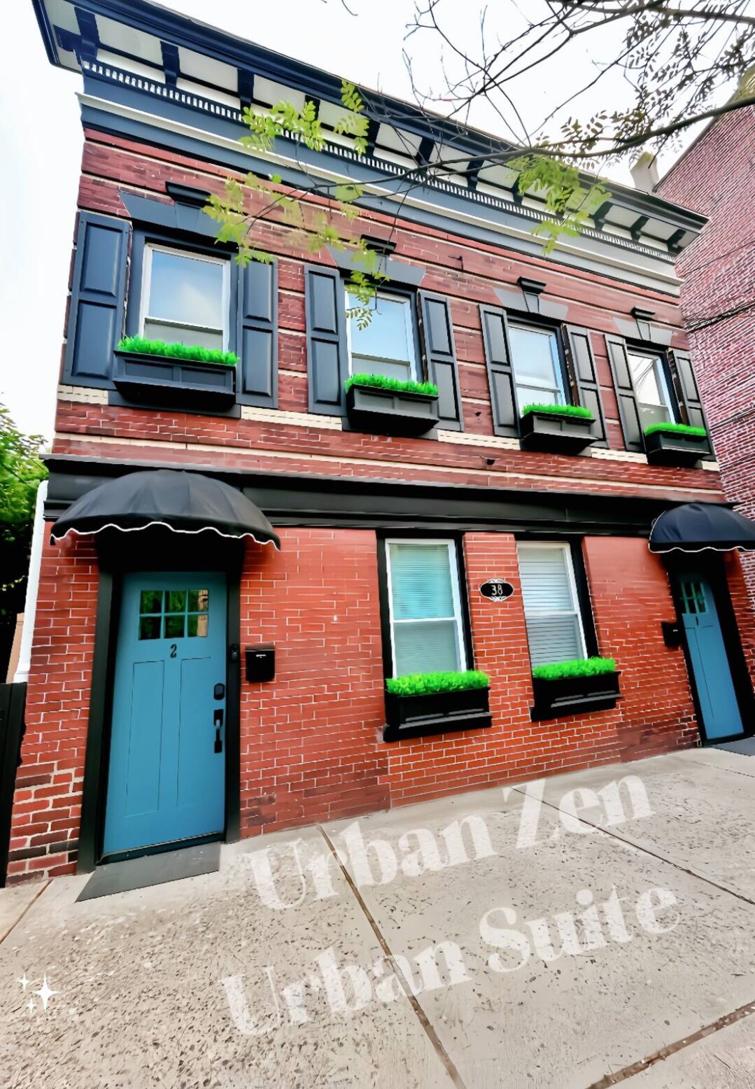 A two-story brick building with a blue door and windows with green plants.