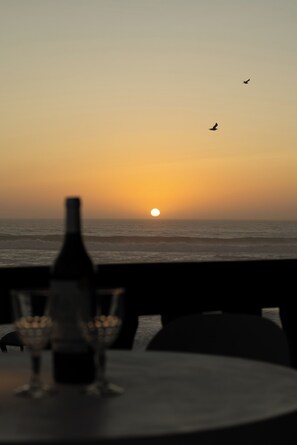 A table with a bottle and glasses, overlooking the ocean at sunset. - Beachfront chalet with walking access to the beach (Marinha Grande)