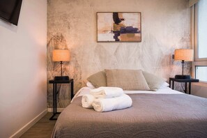 Une chambre d’hôtel avec un lit, deux lampes de chevet, un tableau au mur et une fenêtre.