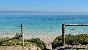 Ein Strand mit klarem, blauem Wasser, einem Sandstrand und einer Holzumzäunung.