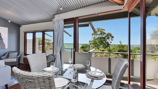 Ein Balkon mit Korbmöbeln, einem Glastisch und Blick auf das Meer.