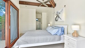 Ein Schlafzimmer mit Bett, Nachttischlampen, Deckenventilator und Blick ins Badezimmer.