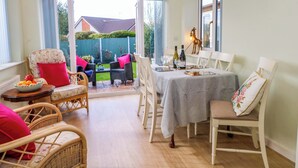 A dining area with a table set for two, surrounded by wicker chairs and a sofa with red cushions. - The Warren (Chester)