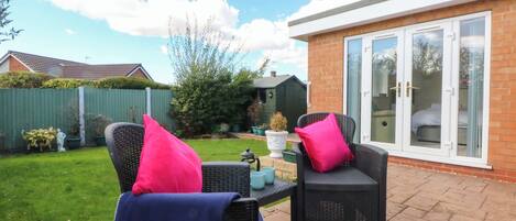 An outdoor patio area with wicker furniture and a glass door leading to a room.