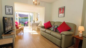 A living room with a sofa, a TV, a table, and a chair. There is a window and a door leading to an outdoor area. - The Warren (Chester)