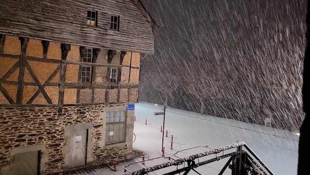 A traditional half-timbered building with a stone foundation, a sign indicating a restaurant, and a snowy slope in the background.