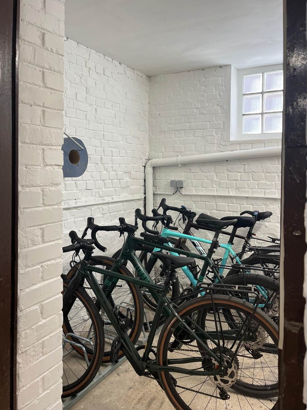 Una habitación con paredes de ladrillo blanco, una ventana y un aparcamiento para bicicletas con varias bicicletas.