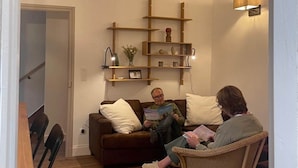 A living room with a brown sofa, a wicker chair, and a wall-mounted shelf with decorative items.