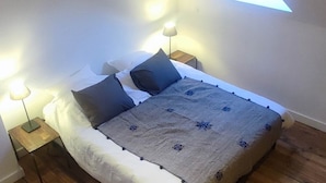 A bedroom with a bed, two bedside lamps, a skylight, and wooden flooring.