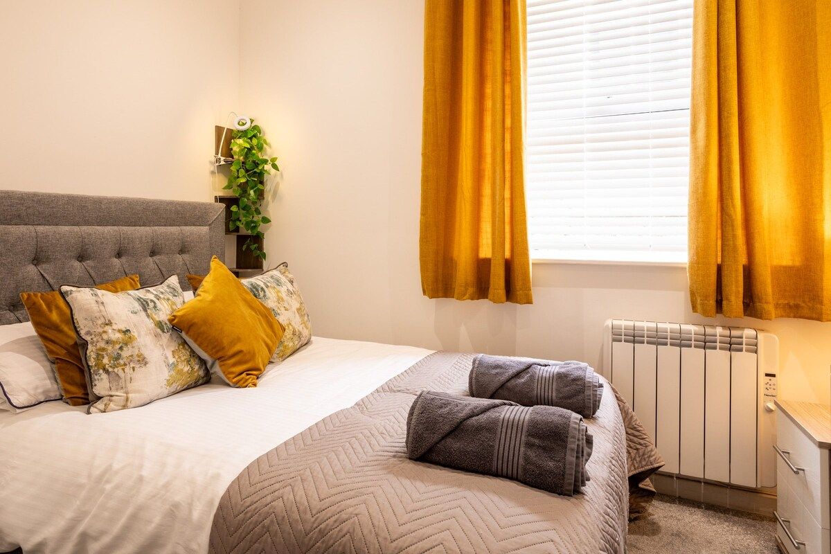 A bedroom with a bed, a radiator, a plant, and curtains.