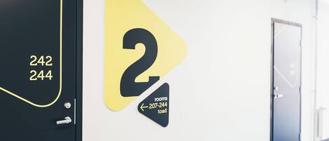 Pasillo de hotel con una puerta marcada '242 244' y un cartel en la pared que indica 'habitaciones 2' junto con un número de contacto.