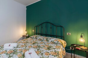 A bedroom with a bed, two bedside tables, a nightstand, and a wall-mounted light fixture.
