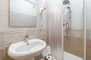 A bathroom with a sink, a hairdryer, a shower, and a mirror.