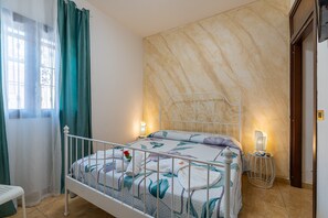A bed with a floral bedspread, a bedside table with a lamp, and a window with curtains.