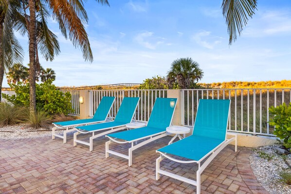 A poolside area with four blue lounge chairs and a white railing.