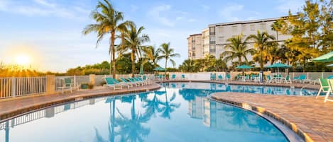 A swimming pool with lounge chairs and palm trees, surrounded by a building.