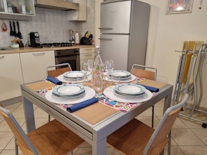 A dining table set with plates, glasses, and cutlery, surrounded by chairs. - Freddy's House Apartment (Loano)