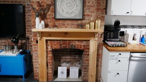 Una sala de estar acogedora con chimenea de ladrillo, televisor montado y cafetera.
