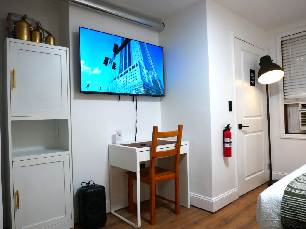 Een kamer met een bureau, stoel, televisie, witte kasten en een brandblusser.