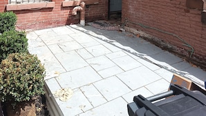 Un edificio de ladrillo con un pequeño jardín delantero, una escalera de metal y una puerta con buzón.