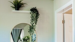 Una habitación con un espejo ovalado grande, un estante pequeño con una planta y una puerta a la derecha.