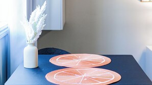 Una pequeña mesa con dos individuales naranja, un florero blanco con flores blancas y una silla azul oscuro.
