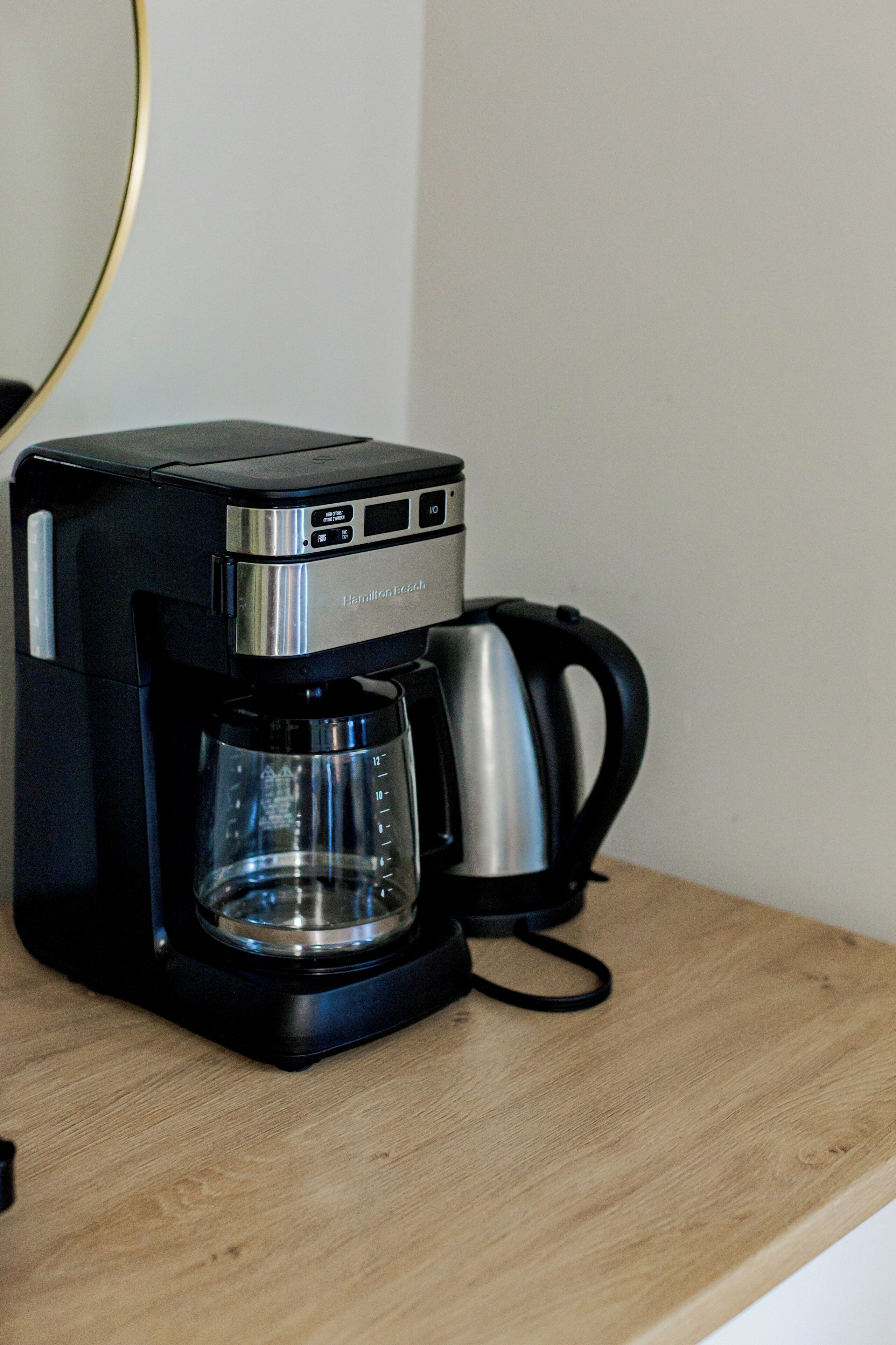 Een zwarte koffiezetapparaat met een glazen kan en een roestvrijstalen pot op een houten oppervlak.