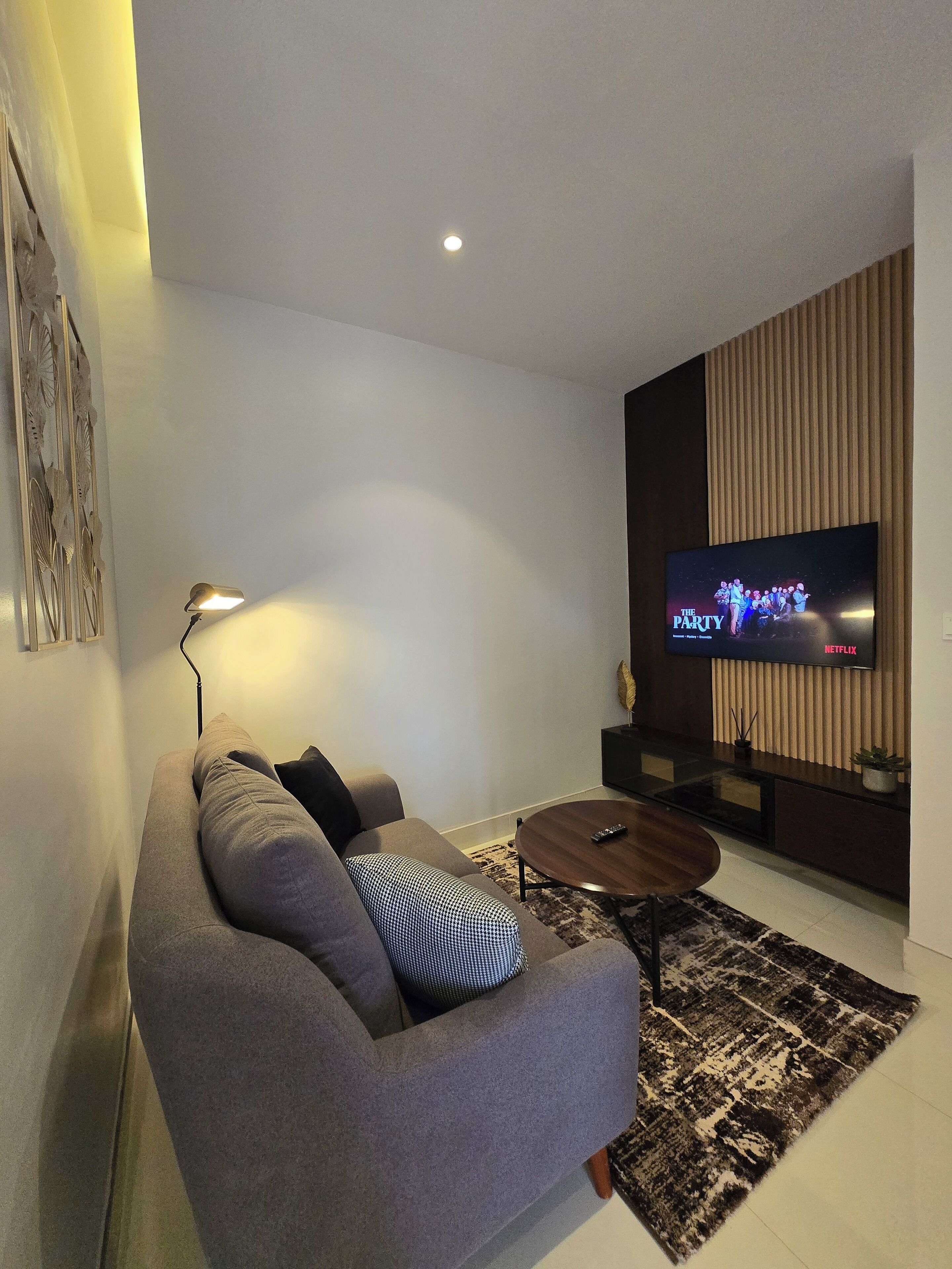 A modern living room with a grey sofa, a coffee table, and a flat-screen TV mounted on the wall.