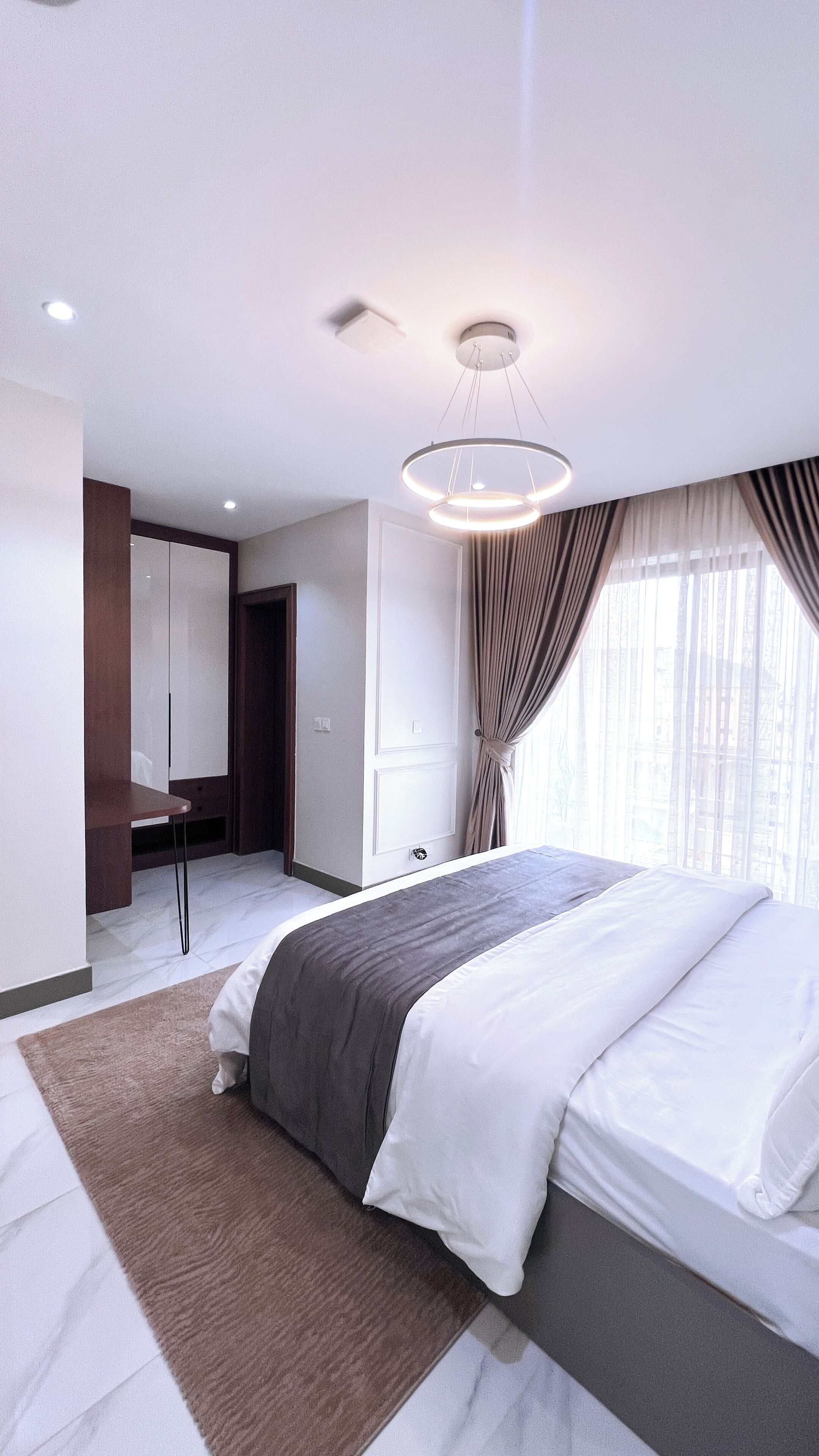A modern bedroom with a large bed, a bedside table, a wardrobe, and a ceiling light fixture.