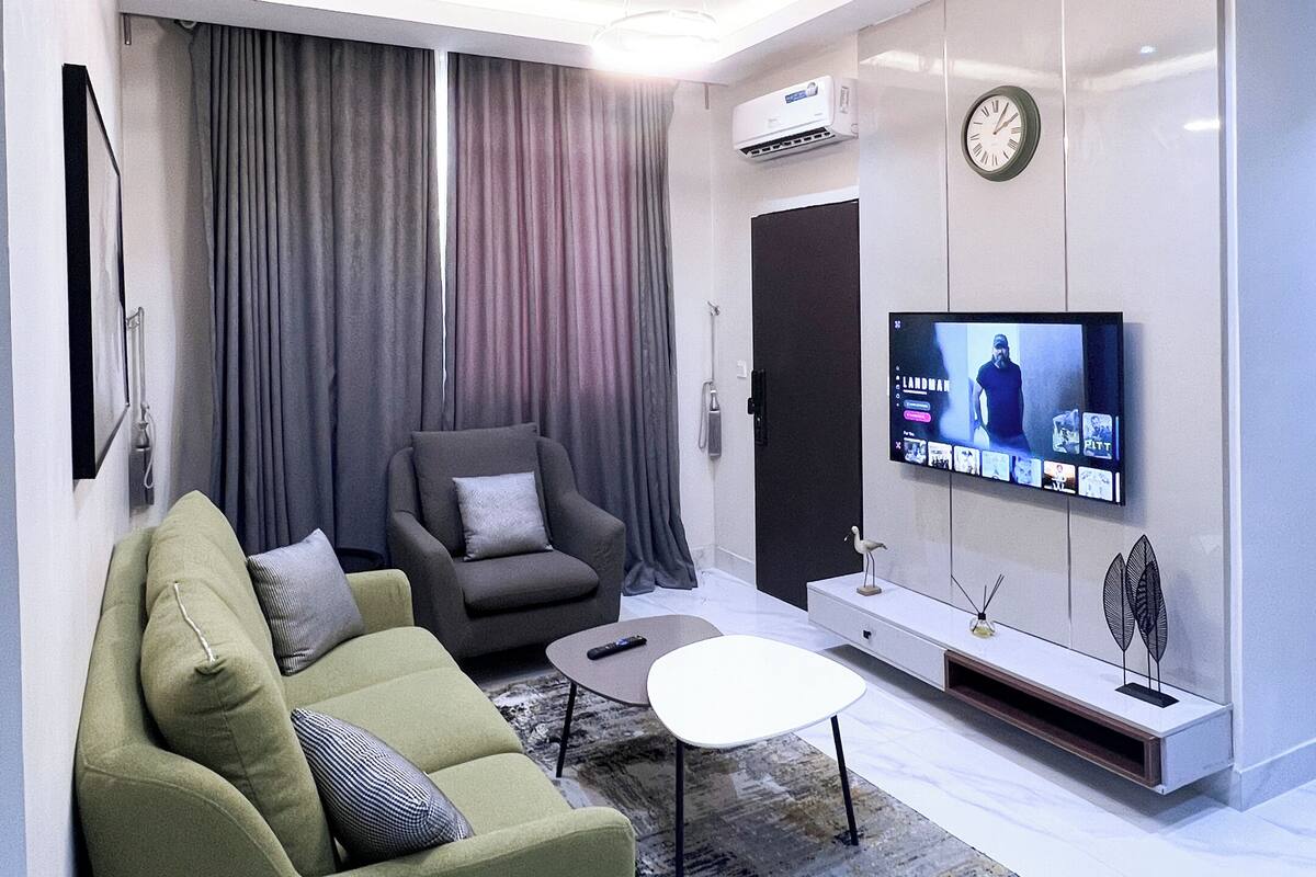 A modern living room with a sofa, armchair, coffee table, and a flat-screen TV mounted on the wall.