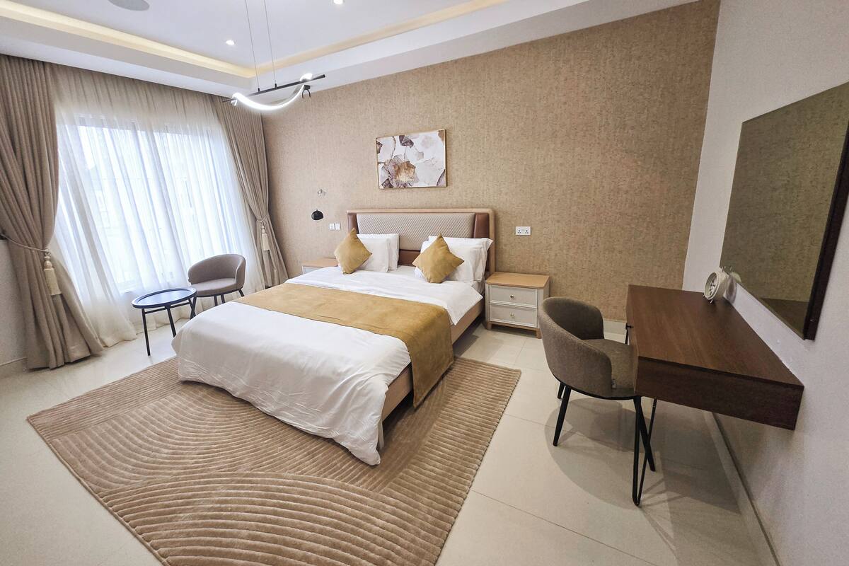 A modern hotel room with a large bed, a desk, a chair, and a view of the city through the window.
