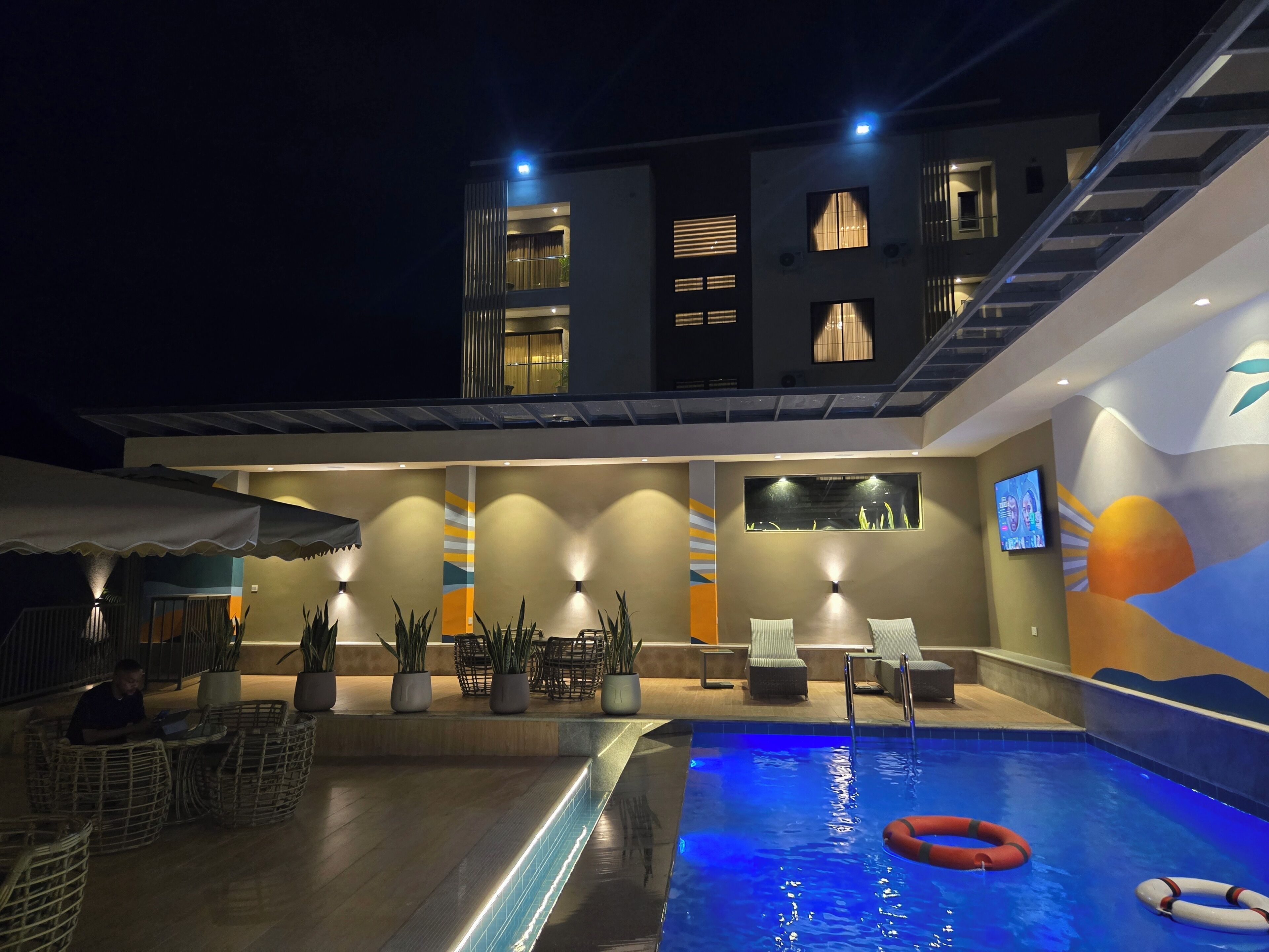 A modern outdoor pool area with lounge seating, a swimming pool, and a building with multiple balconies and windows.