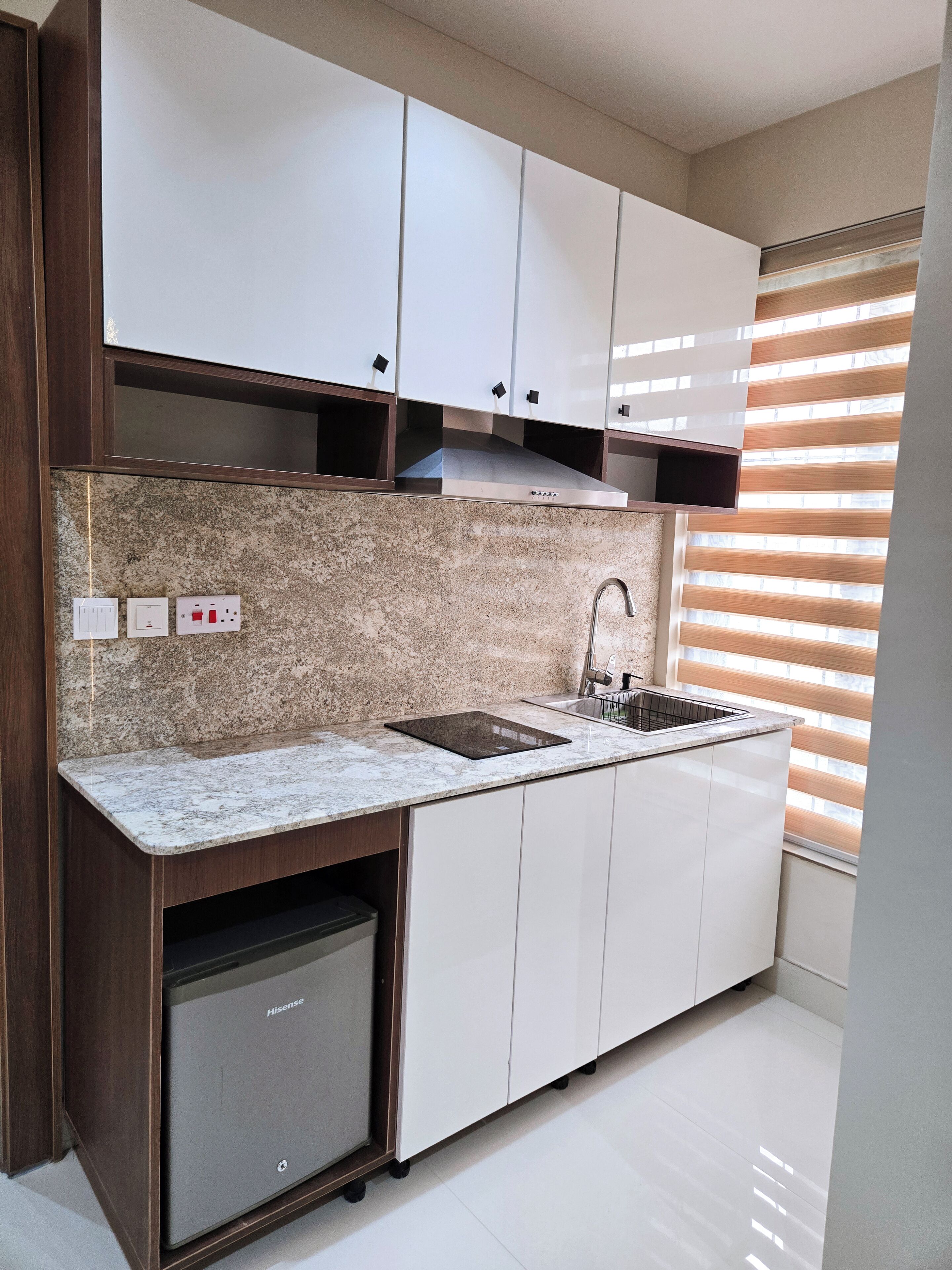A modern kitchen with white cabinets, granite countertops, a stainless steel range hood, a sink, and a built-in dishwasher.