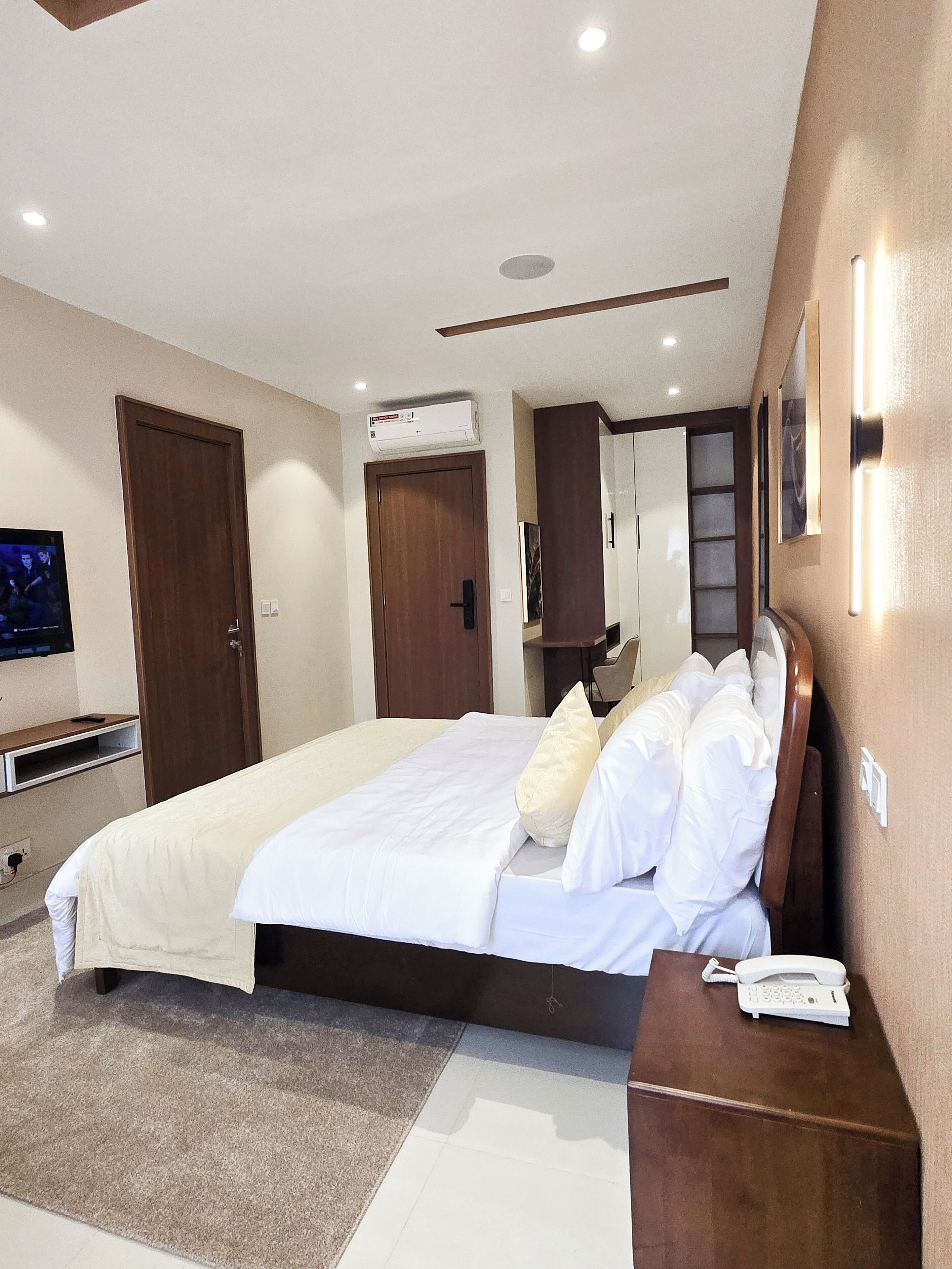 A hotel room with a large bed, a bedside telephone, and a television on the left wall.