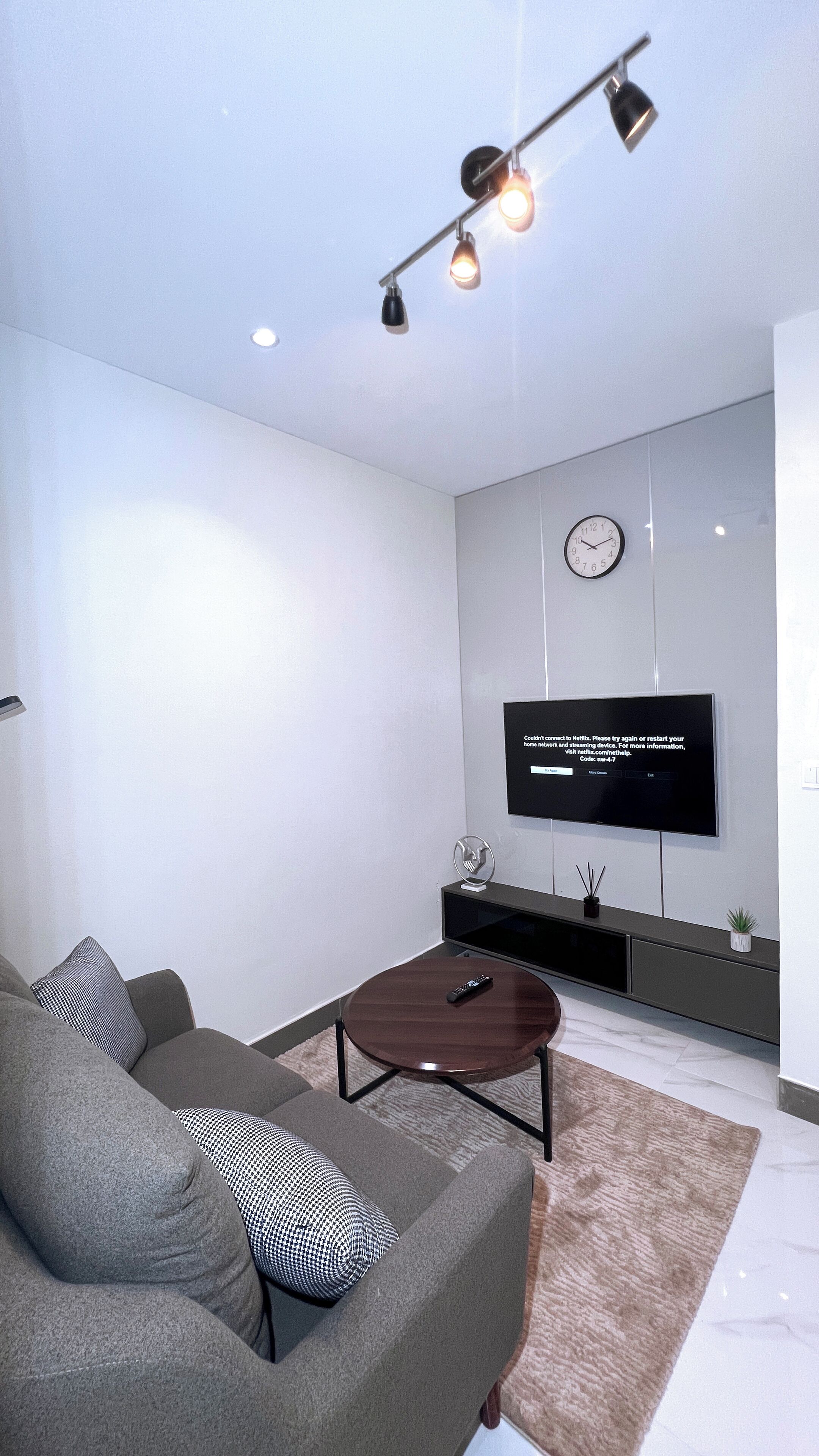 Ein modernes Wohnzimmer mit einem grauen Sofa, einem kleinen Couchtisch und einem an der Wand befestigten Flachbildfernseher.